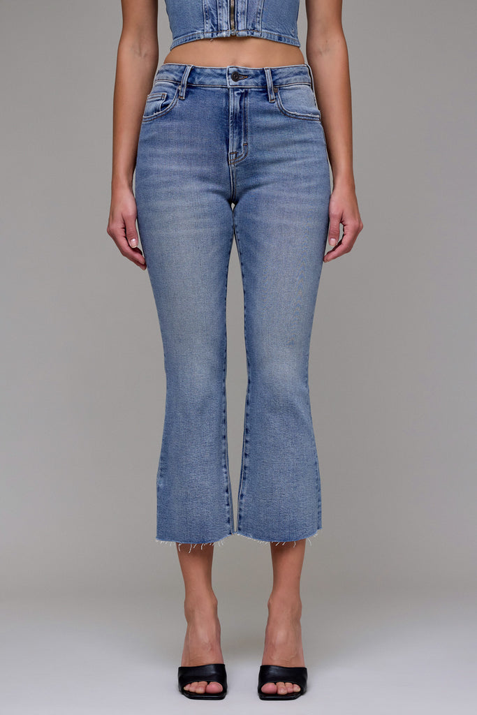 Model in Ryan Cropped Bootcut Jeans by Hidden Jeans, light wash, high-waisted, flared, raw hem, with black mules.