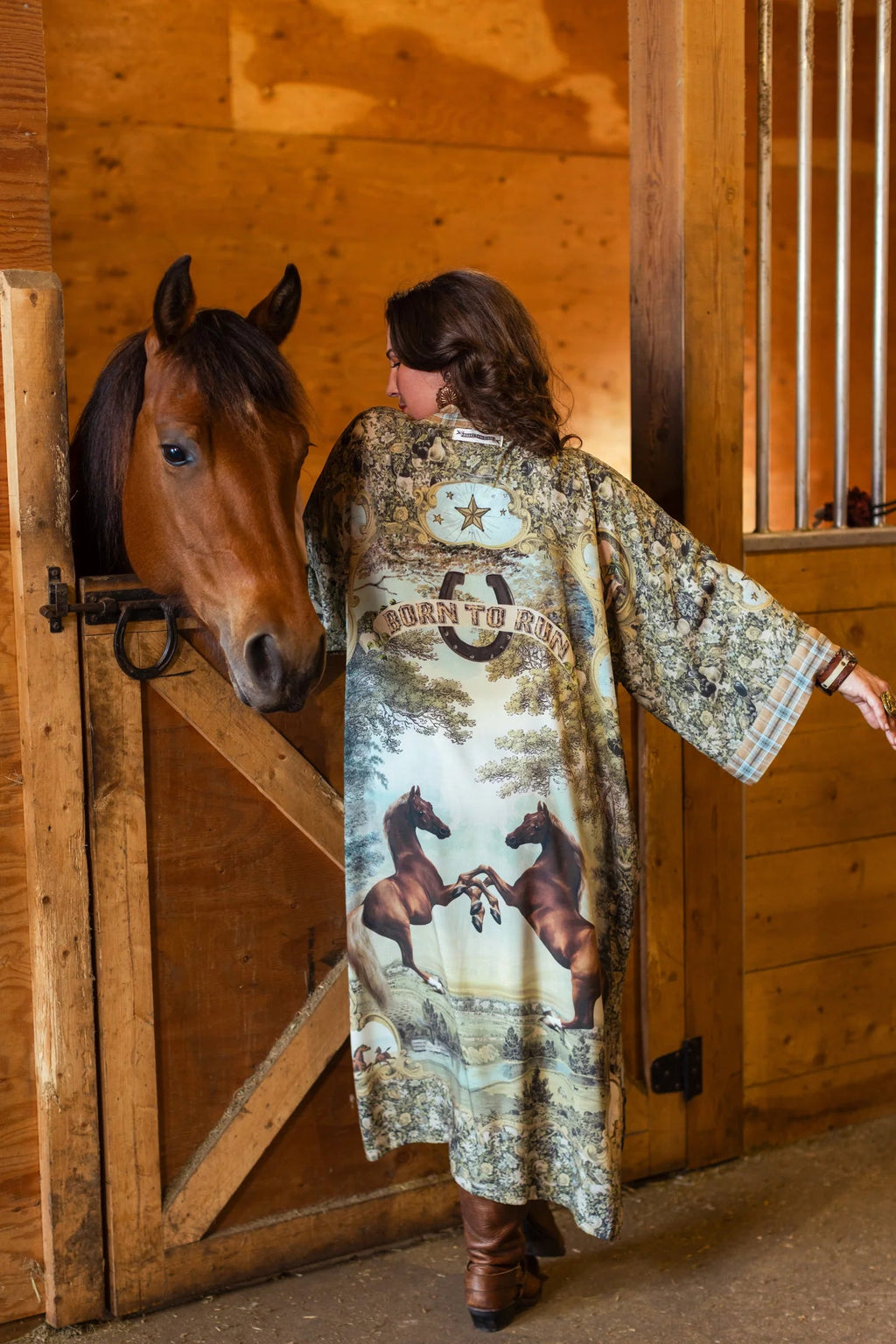 Woman in a Market of Stars 'Born To Run Opera Duster' with horse print, standing with a horse in a stable.
