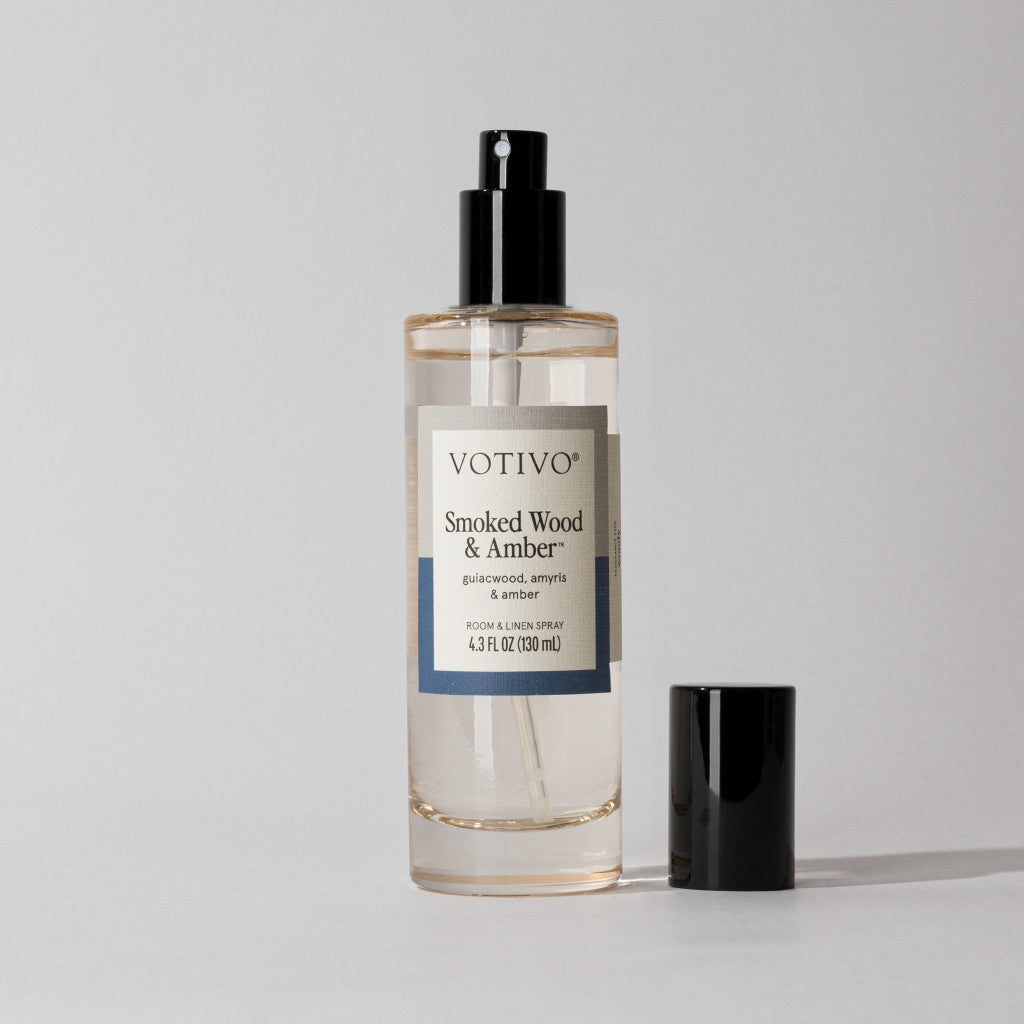 Votivo Smoked Wood & Amber Room & Linen Spray in a clear bottle with its black cap next to it.