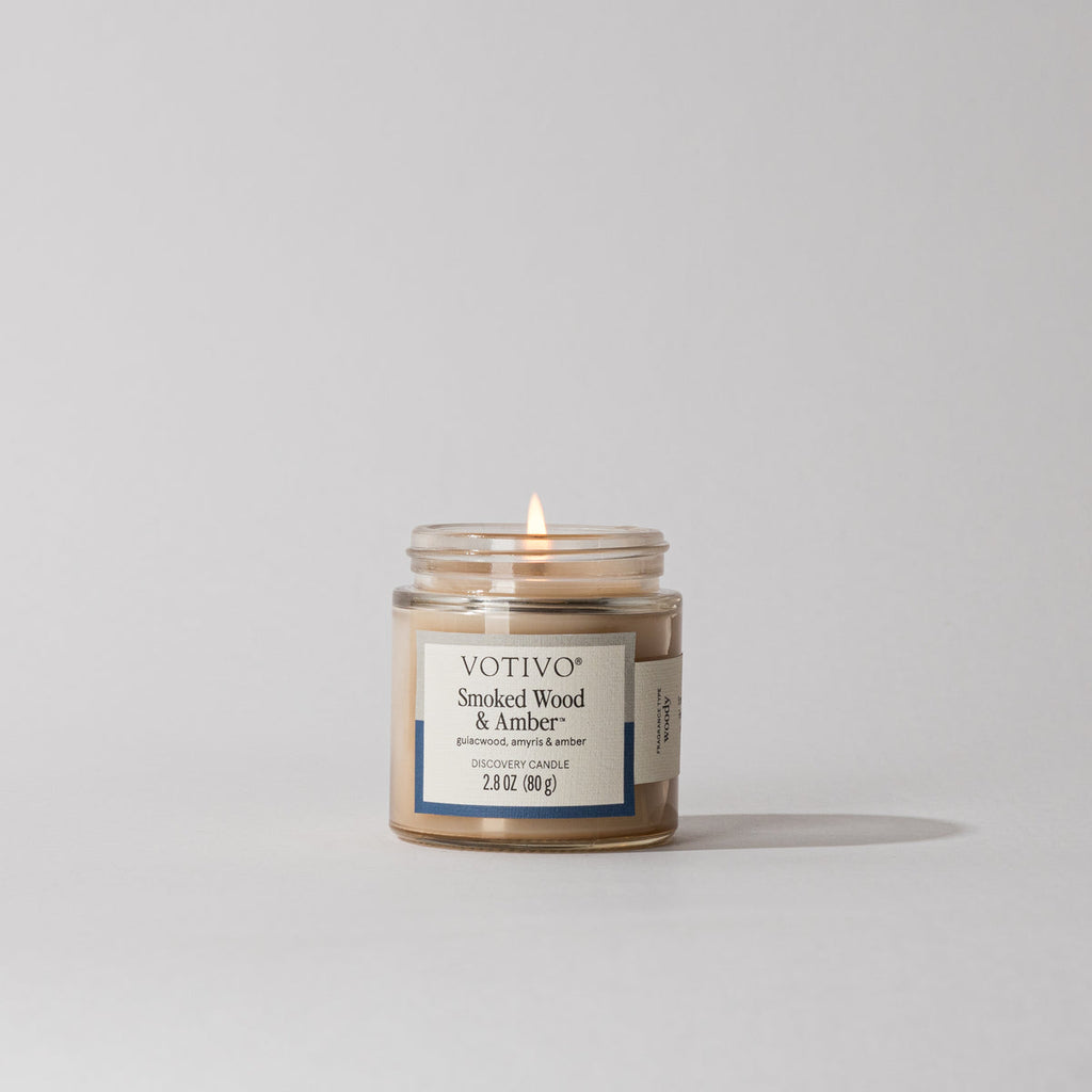 Votivo Smoked Wood & Amber Aromatic Candle, 2.8 oz, in a clear glass jar with a lit wick on a white background.