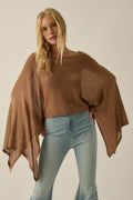 Blonde woman in Promesa Sheer to Stay Knit Poncho Sweater in Taupe with wide sleeves and light blue jeans.