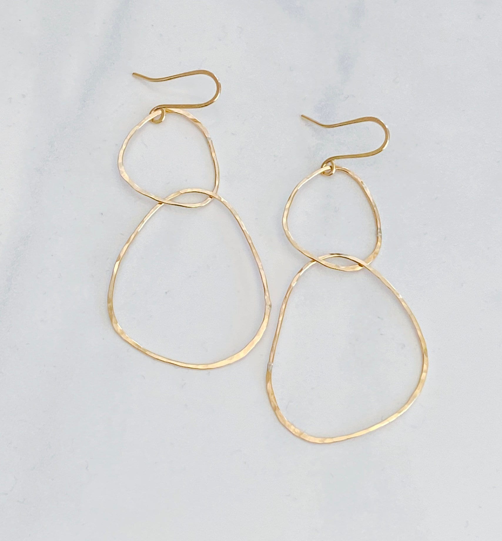 bonnieboardman River Rock Earrings Sterling Silver, gold hammered irregular hoop dangle earrings on a white surface.