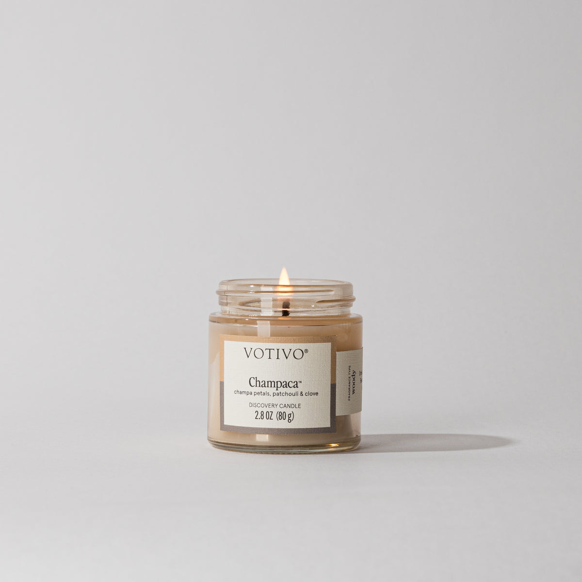 Lit Votivo Champaca Discovery Candle in a glass jar, featuring champa petals, patchouli & clove scent.