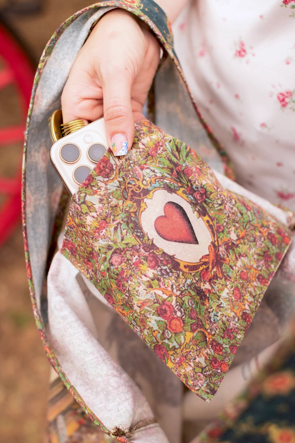 A hand putting a white phone into the Love Revolution Market Tote by Market of Stars, featuring a colorful floral heart design.