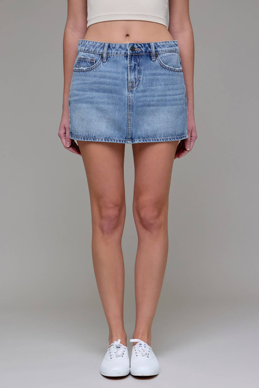 Model wearing Peyton Micro Mini Denim Skirt from Hidden Jeans, light blue wash, micro mini length, distressed hem, and white sneakers.