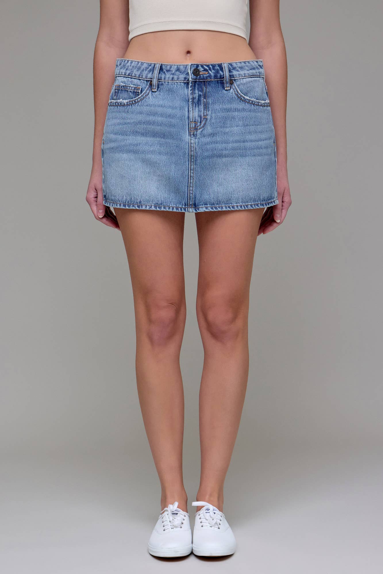 Model wearing Peyton Micro Mini Denim Skirt from Hidden Jeans, light blue wash, micro mini length, distressed hem, and white sneakers.