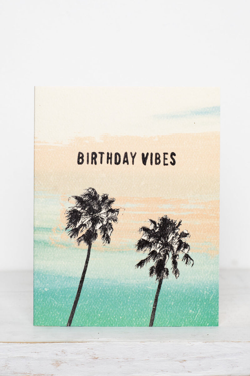 "Birthday Vibes" palm tree greeting card by Daydream Prints featuring two black palm trees against a peach and teal sunset.