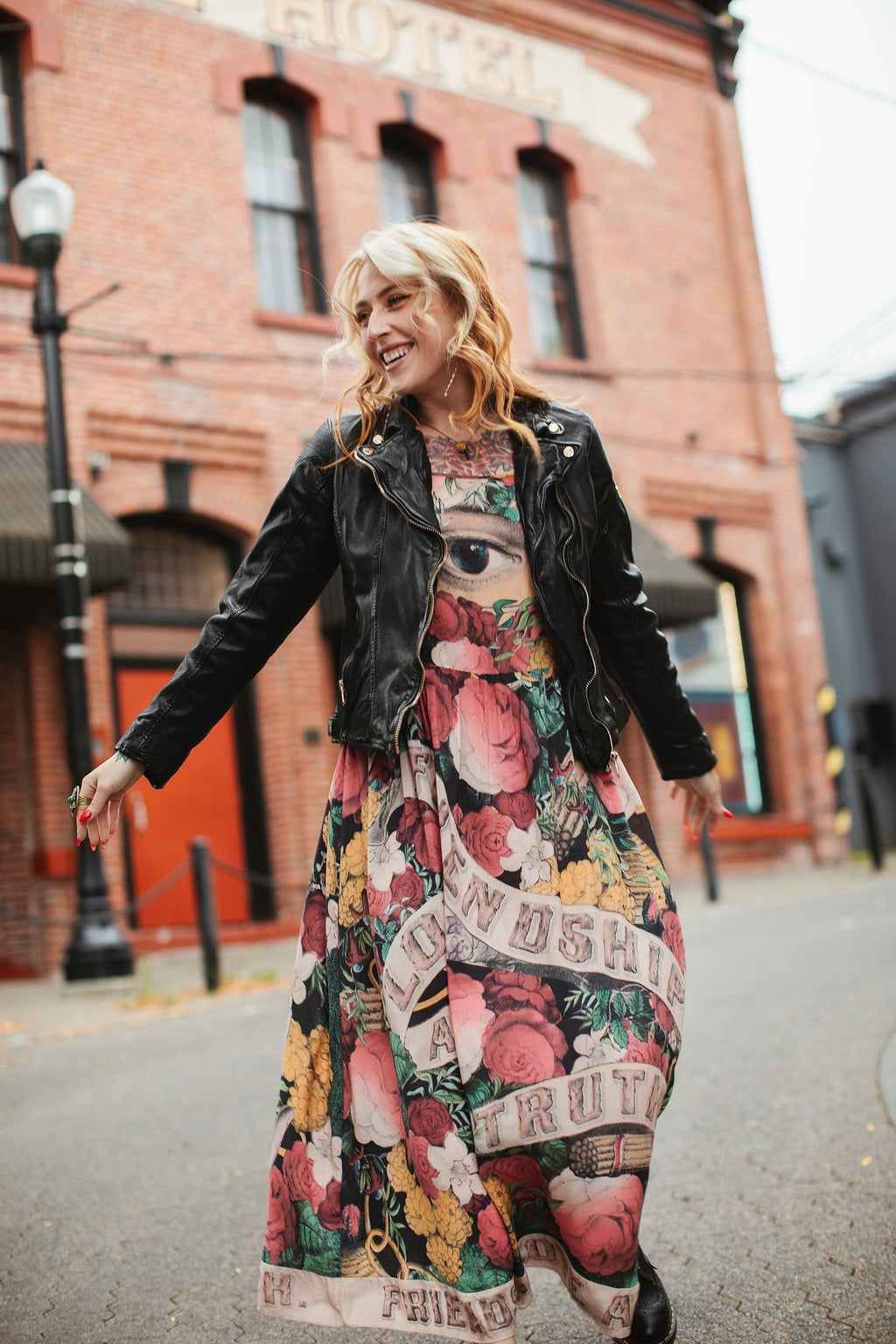 Smiling woman in 'Friendship Love & Truth Bohéme Slip Dress' by Market of Stars, black jacket, floral eye print.