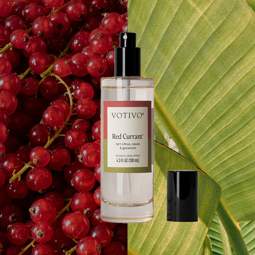 Votivo Red Currant Room & Linen Spray bottle against a vibrant background of red currants and a green leaf.