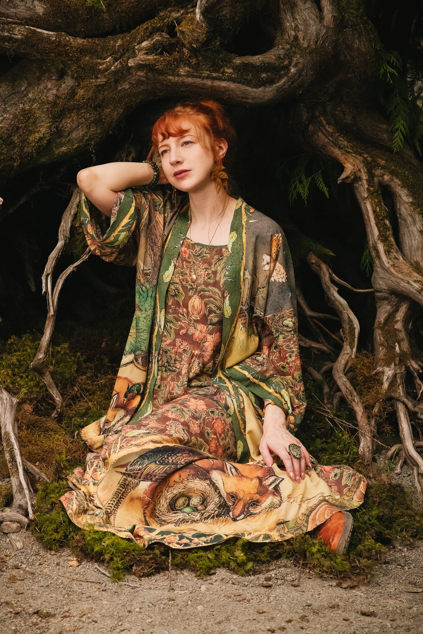 Market of Stars Woodland Wisdom Bohéme Slip Dress. Woman in a nature-inspired dress with foxes & owls, sitting by tree roots.