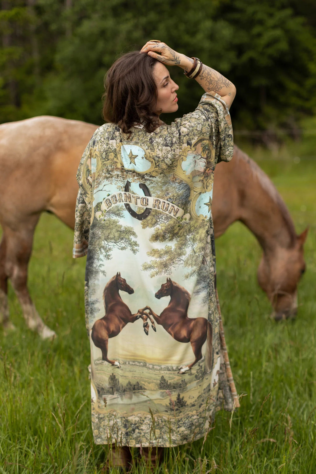 Woman wearing a 'Born To Run Opera Duster' by Market of Stars, featuring horse print, in a field with horses.