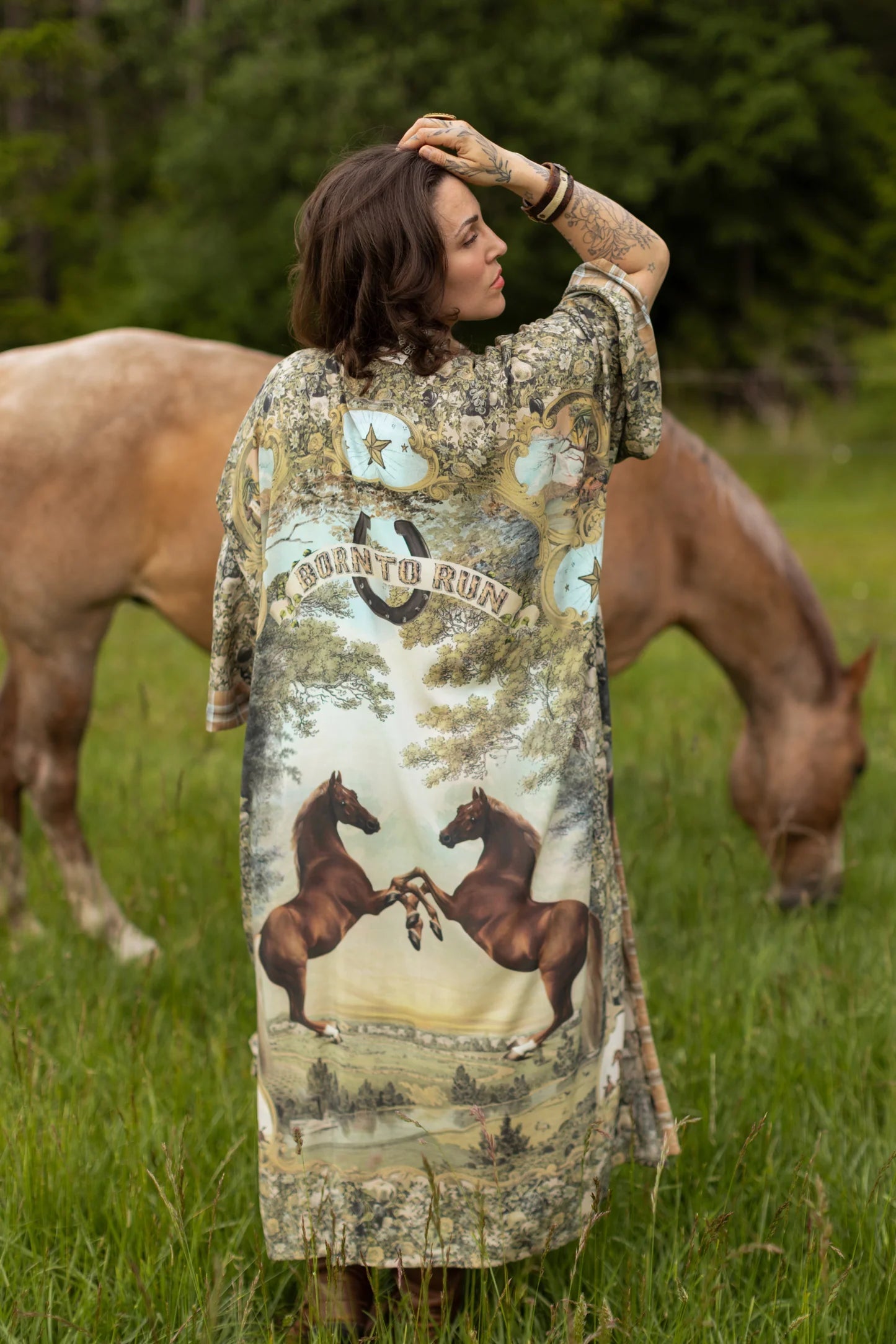 Woman wearing a 'Born To Run Opera Duster' by Market of Stars, featuring horse print, in a field with horses.