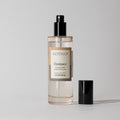 Votivo Champaca Room & Linen Spray bottle with a black spray top and cap. Features champa petals, patchouli, & clove.