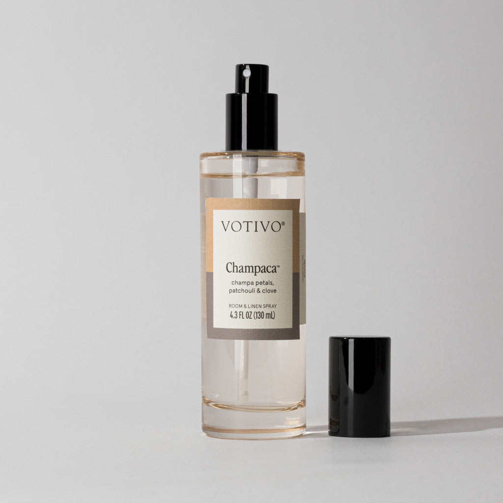 Votivo Champaca Room & Linen Spray bottle with a black spray top and cap. Features champa petals, patchouli, & clove.