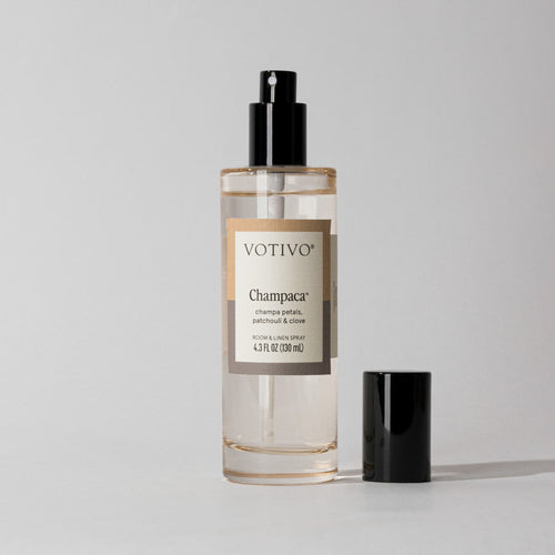 Votivo Champaca Room & Linen Spray bottle with a black spray top and cap. Features champa petals, patchouli, & clove.