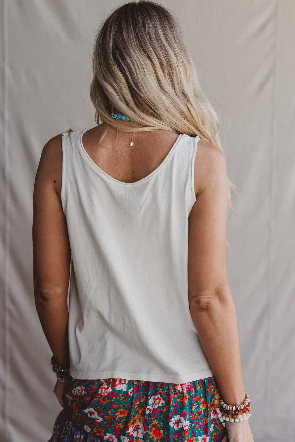Promesa ET1499G Top in White Smoke, a simple white tank top, on a woman from behind, with blonde hair and a turquoise necklace.