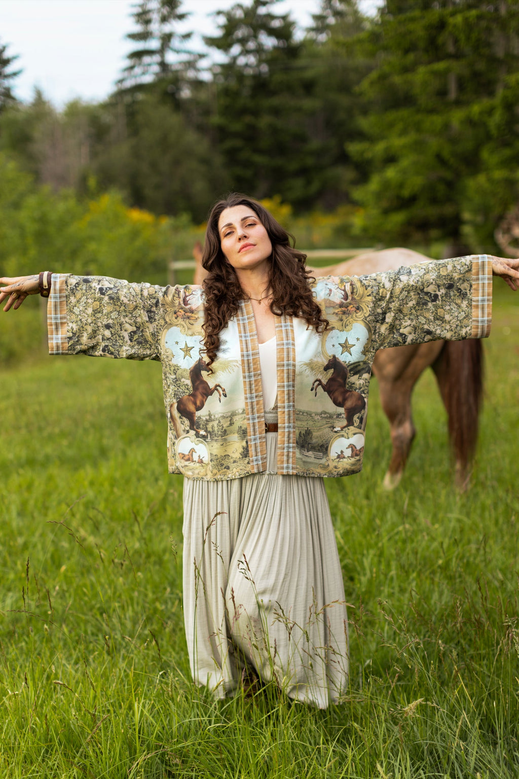 Woman wearing Born To Run Pixie Duster by Market of Stars, featuring horse design, arms outstretched in a green field with a horse.