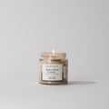 Votivo Smoked Wood & Amber Discovery Candle lit, in a clear glass jar, on a white background. Guaiacwood, amyris, amber.