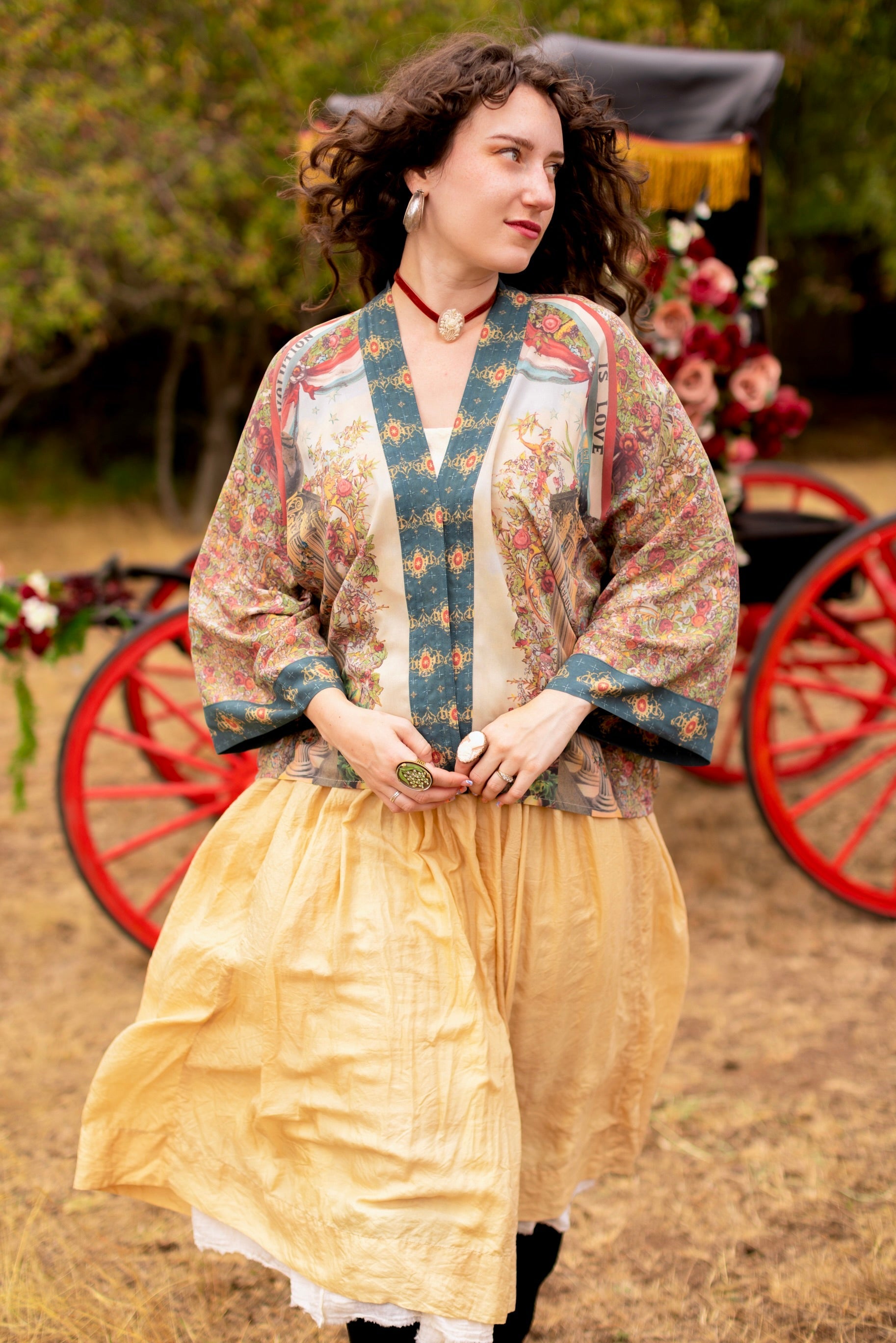 Woman wears Love Revolution Pixie Duster from Market of Stars, featuring colorful floral patterns, with a golden skirt and red cart background.