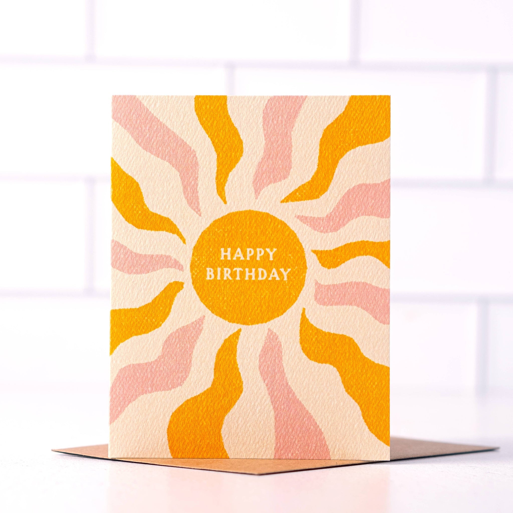 Happy Birthday Boho Sun Card by Daydream Prints. Textured card with orange sun, pink/orange wavy rays, standing on a brown envelope.