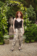 Redhead in Market of Stars Honey & The Moon Artist Pants, a floral botanical print, black top, standing in a garden.