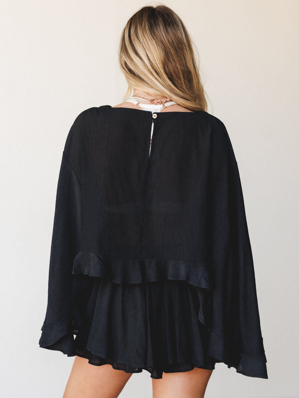L9403T By Together Black Cropped Blouse with long loose sleeves and ruffled hem, shown from the back on a woman.