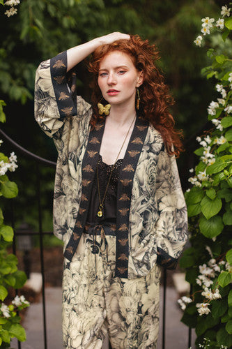 Red-haired model in Market of Stars Honey & The Moon Pixie Duster & pants with bee trim, amidst white flowers.