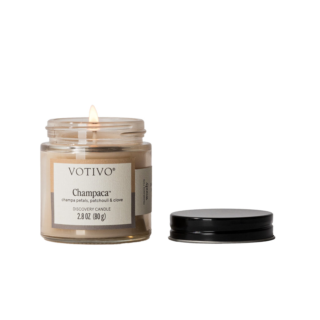 Votivo Champaca Discovery Candle, a woody fragrance with champa petals, patchouli & clove, lit, 2.8 oz, with lid.