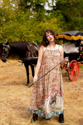 Woman in Market of Stars Love Revolution Bohéme Slip Dress, holding a riding crop, with a horse and carriage behind her.