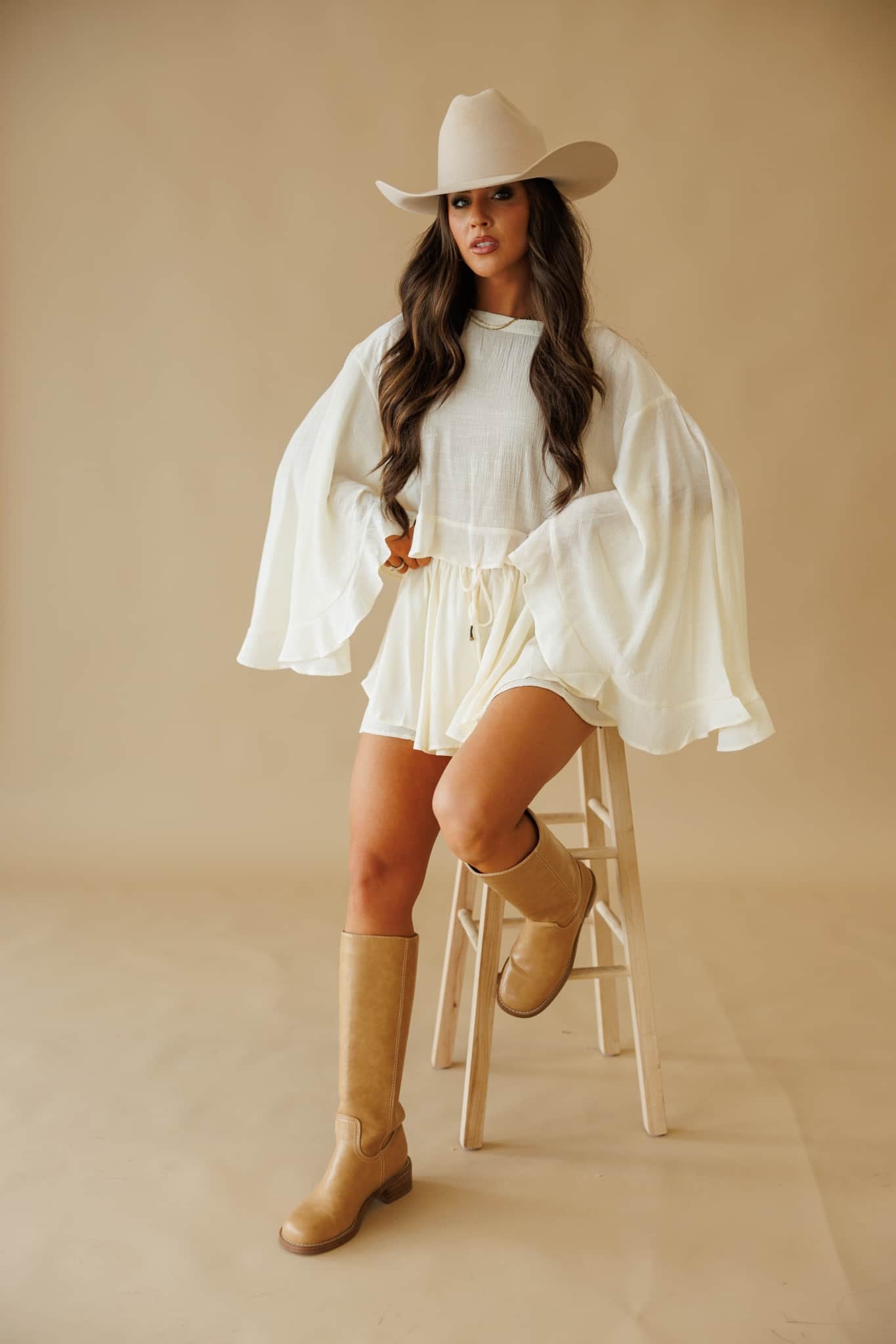 Woman in L9403T Cropped Blouse in Cream by By Together, matching romper, cowboy hat, and tan boots.
