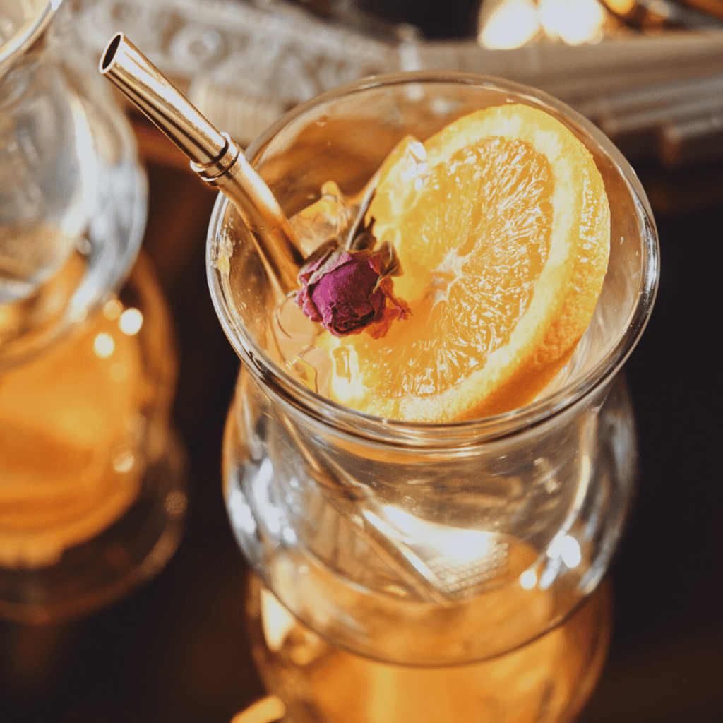 Sips Tea Straw & Strainer Bombilla — Gold | Magic Hour in a glass with an orange slice and rosebud. Perfect for tea.