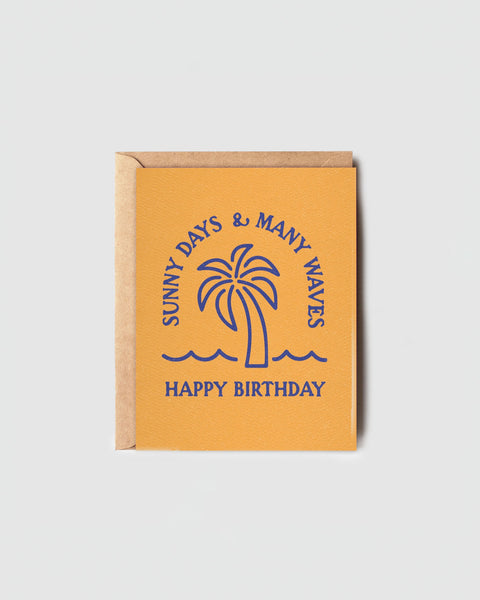 Sunny Days Many Waves Birthday Card by Daydream Prints, featuring a blue palm tree and waves on a yellow background.