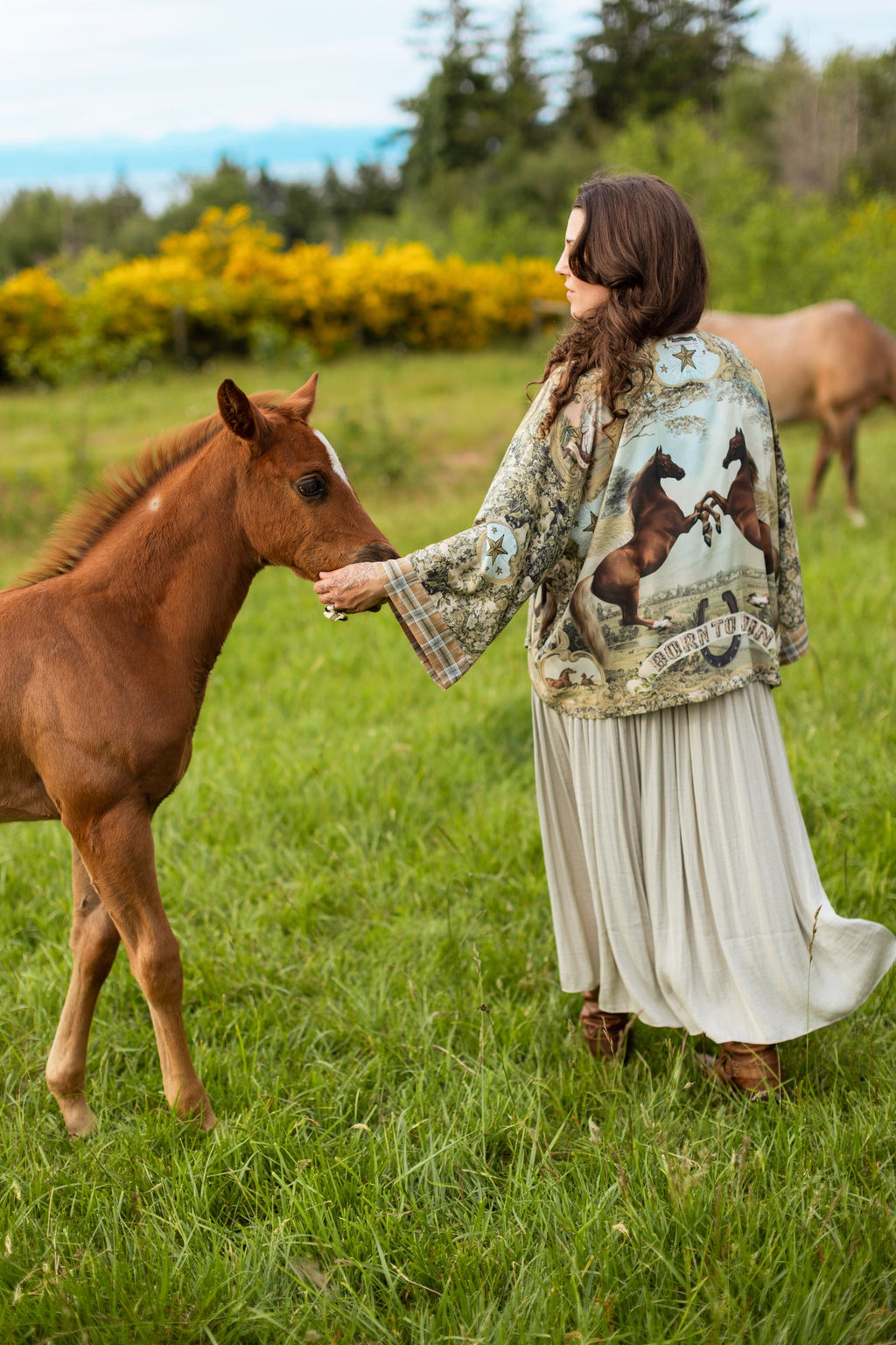 Woman in a 'Born To Run Pixie Duster' by Market of Stars, featuring horse design, gently pets a brown foal in a field.