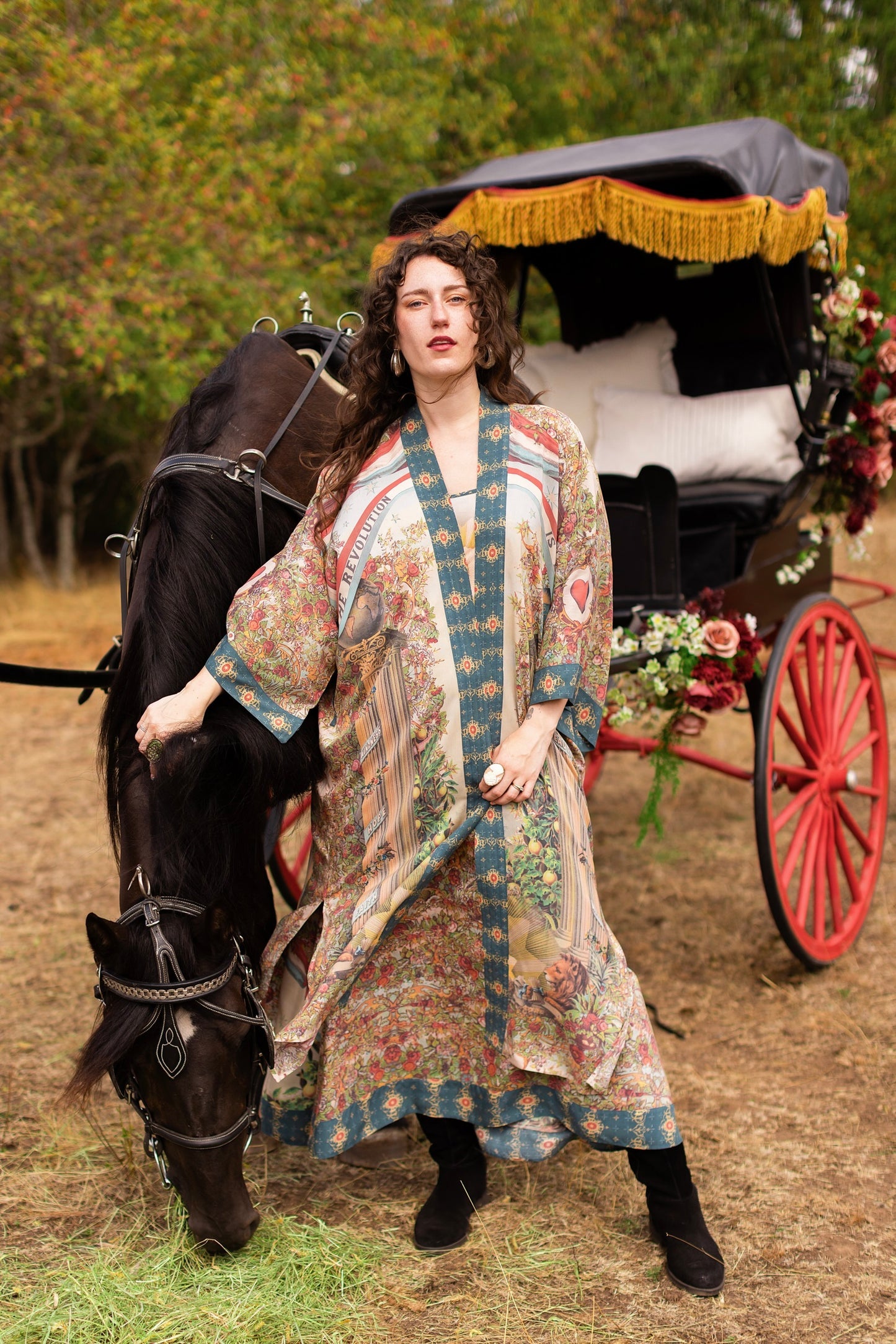 Model wears vibrant floral Market of Stars Love Revolution Opera Duster, standing with a horse and vintage carriage.