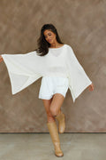 Off-white Promesa Sheer to Stay Knit Poncho Sweater on a model, styled with white shorts and tan boots. Great for layering.