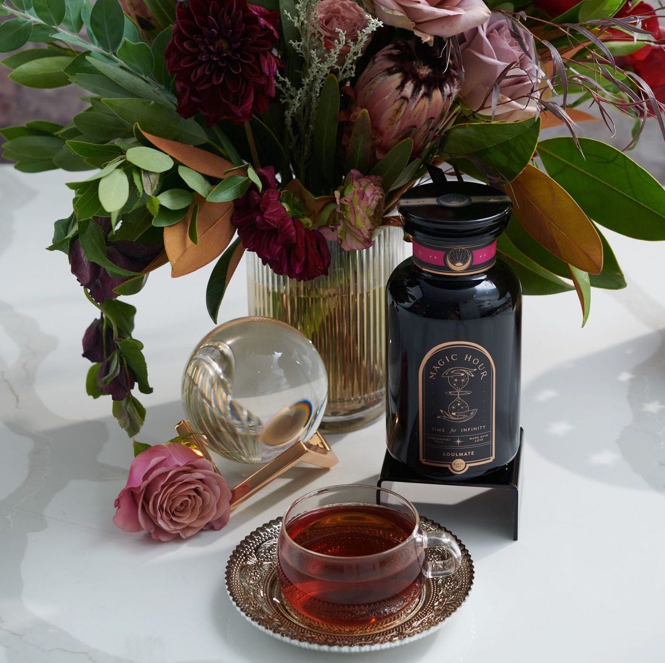 Magic Hour Soulmate Chocolate-Raspberry-Rose Black Tea bottle & cup, pink rose, crystal ball, & floral arrangement.
