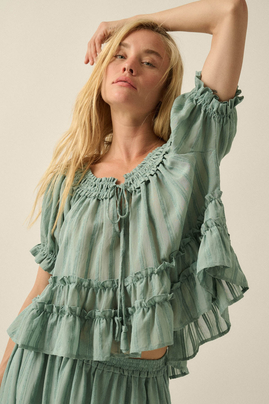 Blonde woman wearing a sheer pine green Precious Days Ruffle Babydoll Top by Promesa with striped pattern and tiered ruffles.