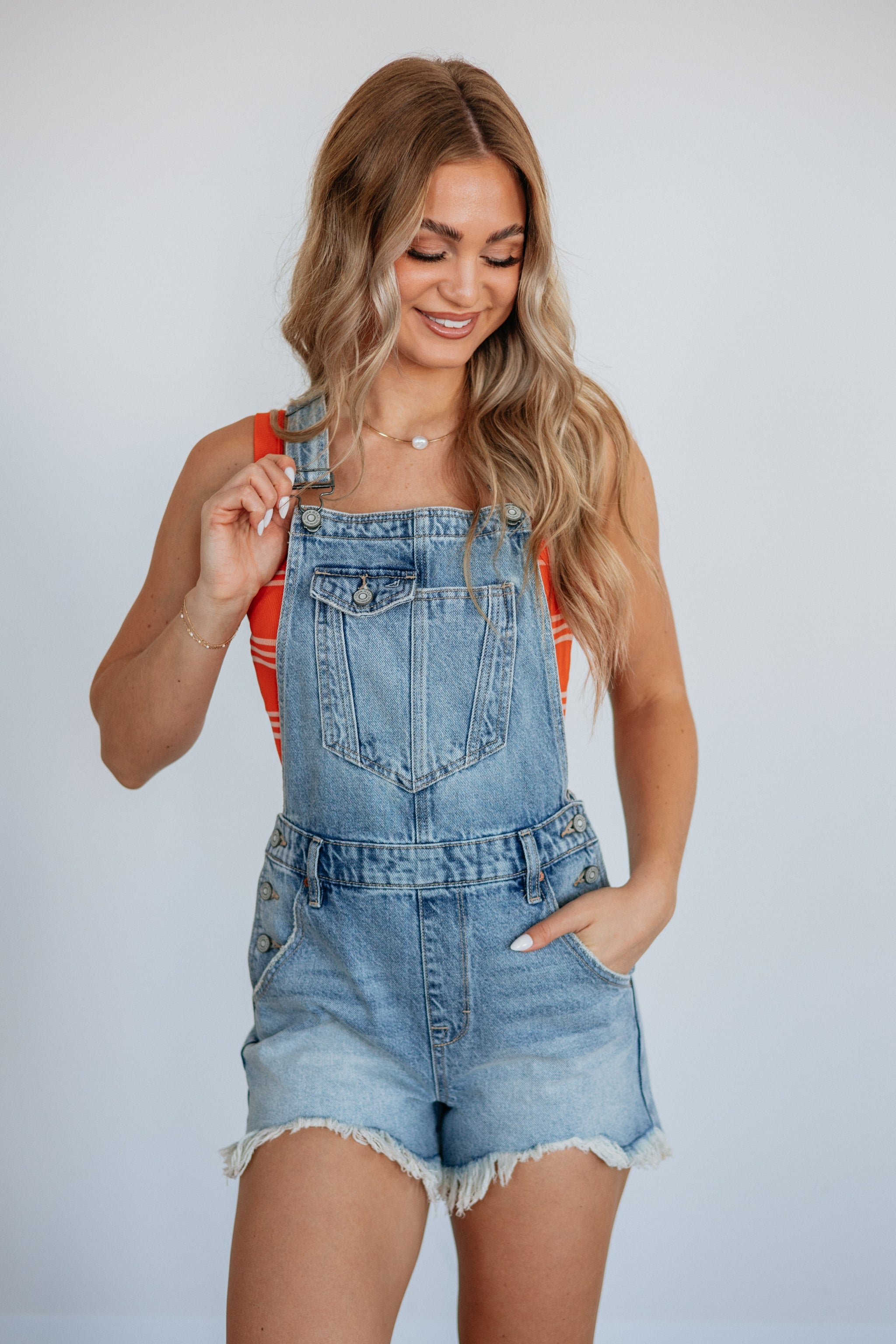 Dylan Classic Denim Shortall by Hidden Jeans. A smiling woman models light wash denim shortalls over an orange striped top.
