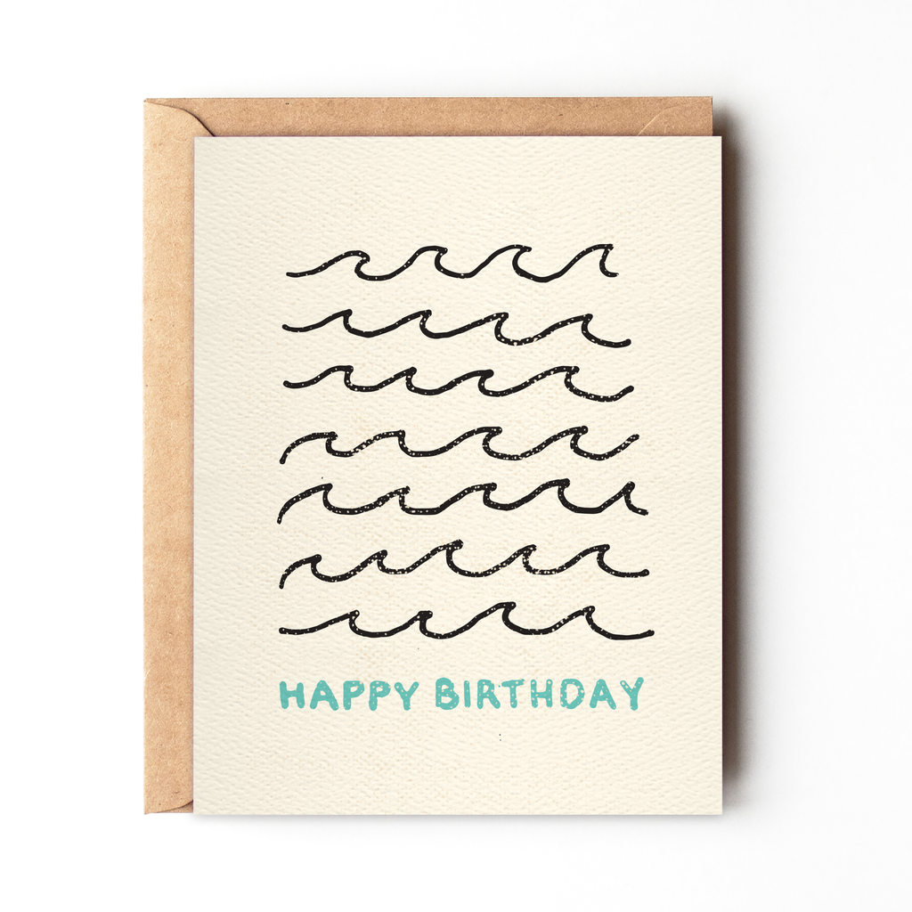 Happy Birthday Wave Card by Daydream Prints. Light cream card with black wave pattern and blue 'Happy Birthday' text, kraft envelope.