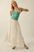 Pretty Precious Ruffle Maxi Skirt — Off White | Promesa. Model wears with a green crop top and tan sandals.