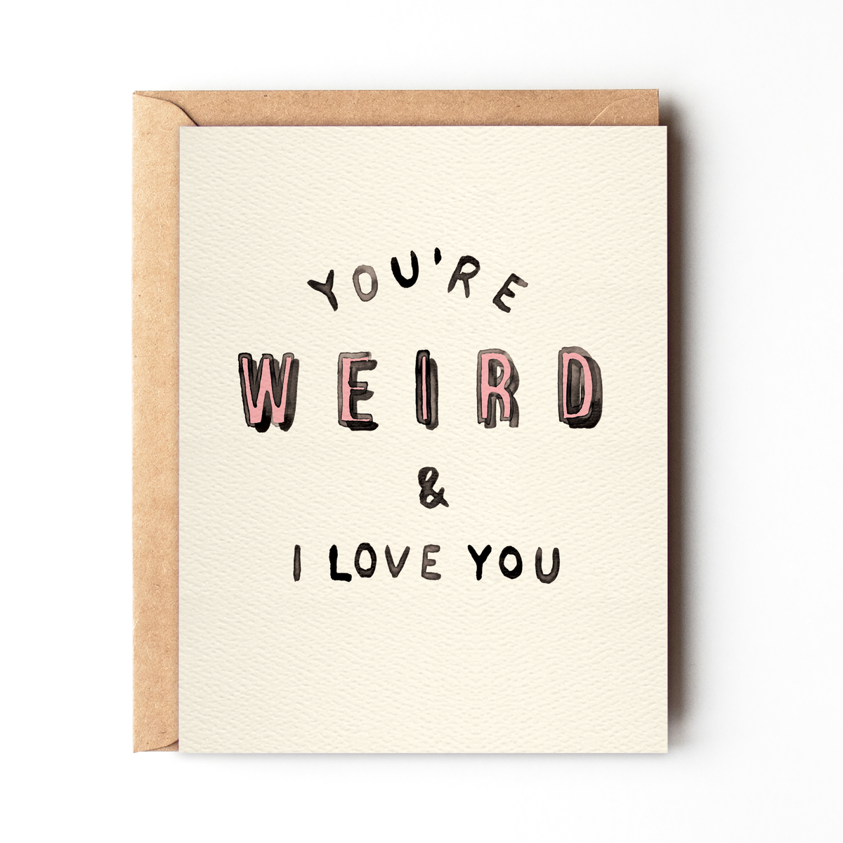 Cream greeting card 'You're Weird & I Love You Card | Daydream Prints' with black and pink handwritten text, kraft envelope.