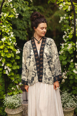 Woman models Market of Stars Honey & The Moon Pixie Duster, a floral and moth-patterned kimono in black, white, and gold.