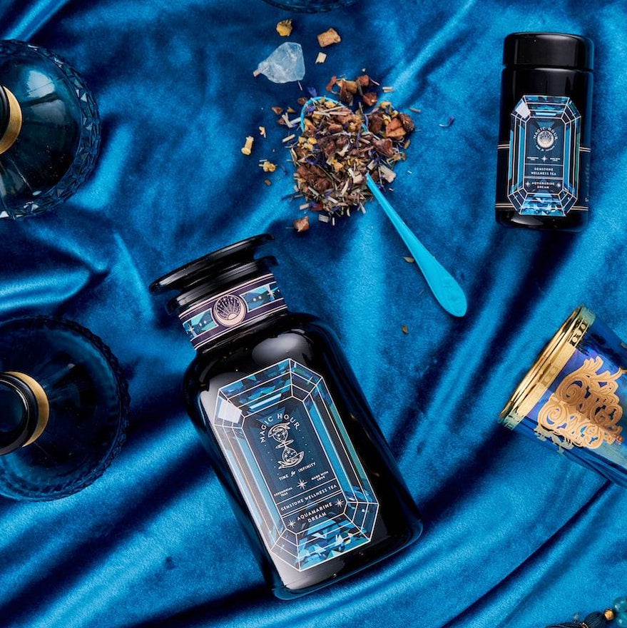 Magic Hour Aquamarine Dream Herbal Adrenal Tonic bottles on blue silk, with loose tea, a spoon, and a crystal.