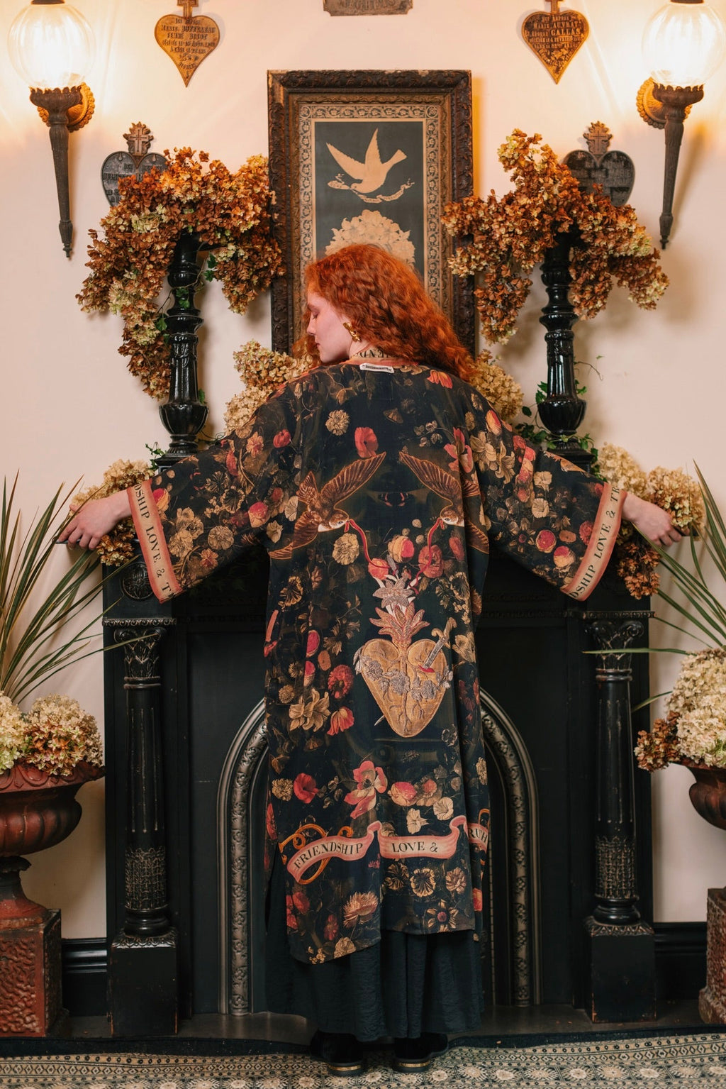 Red-haired woman in Market of Stars Heart of Gold Opera Duster, black with floral, bird, & 'Friendship Love & Truth' heart design.