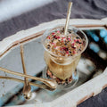 Gold Magic Hour Sips Tea Straw & Strainer Bombilla in a floral tea cup, with two more gold bombillas on a mirrored tray.