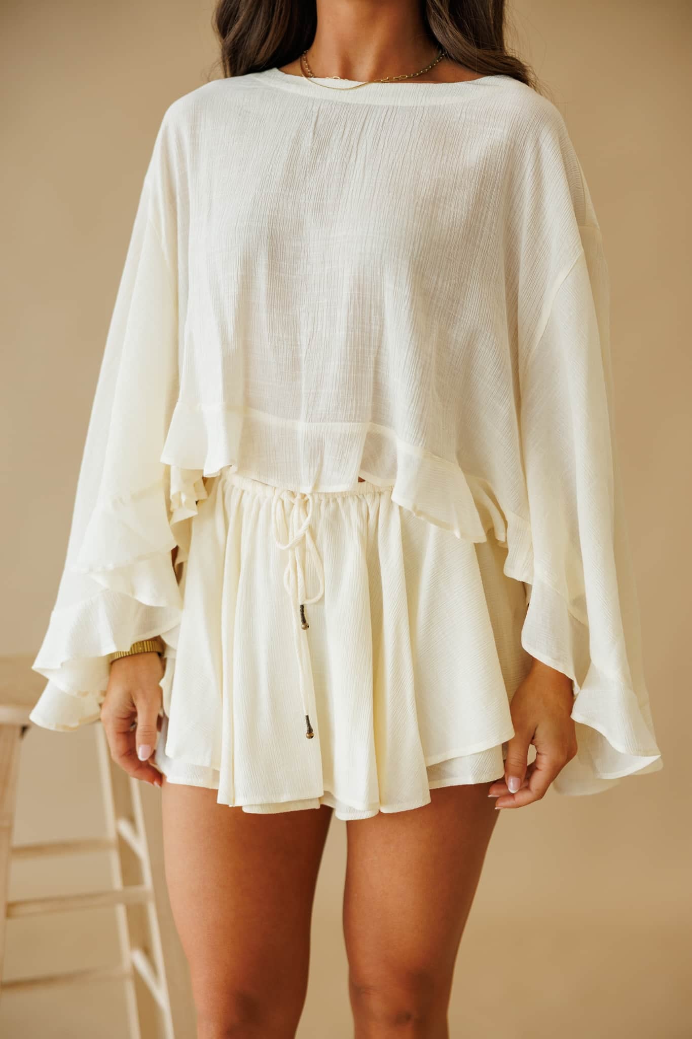 By Together L9403T Cropped Blouse in Cream. Textured, oversized cream top with loose fit, boat neck, and ruffled bell sleeves.