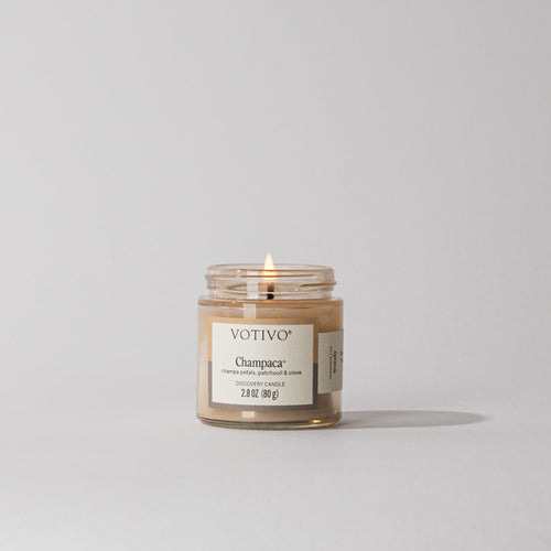 Votivo Champaca Aromatic Candle, discovery candle with a lit wick in a glass jar, on a white background.