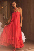 Promesa Roaming Free Cotton Gauze Maxi Dress. Woman in a Red Orange halter dress with smocked bodice, ruffled tiers & eyelet lace.
